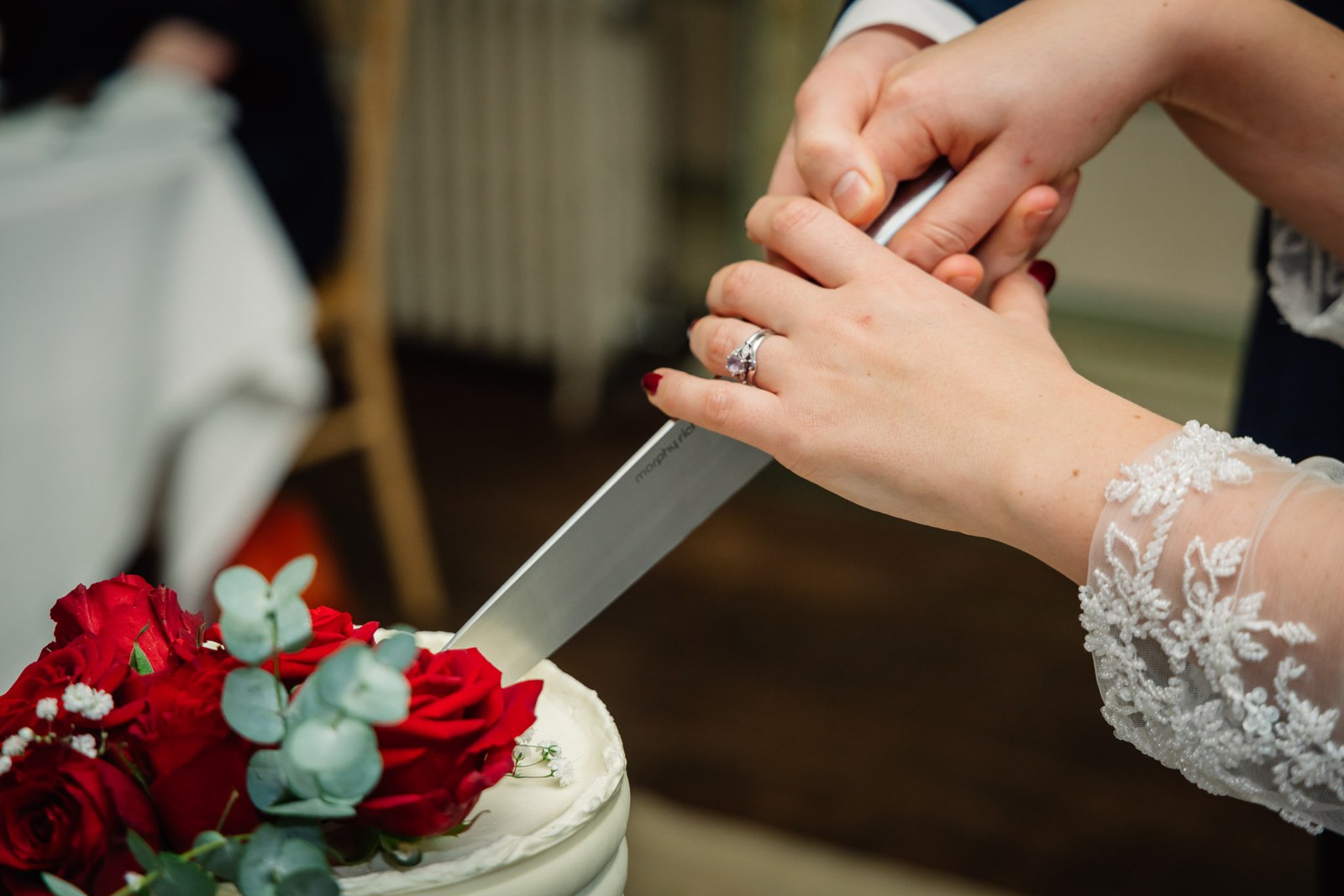 Close-up of the couple's hands cutting the cake, rings and red roses showing