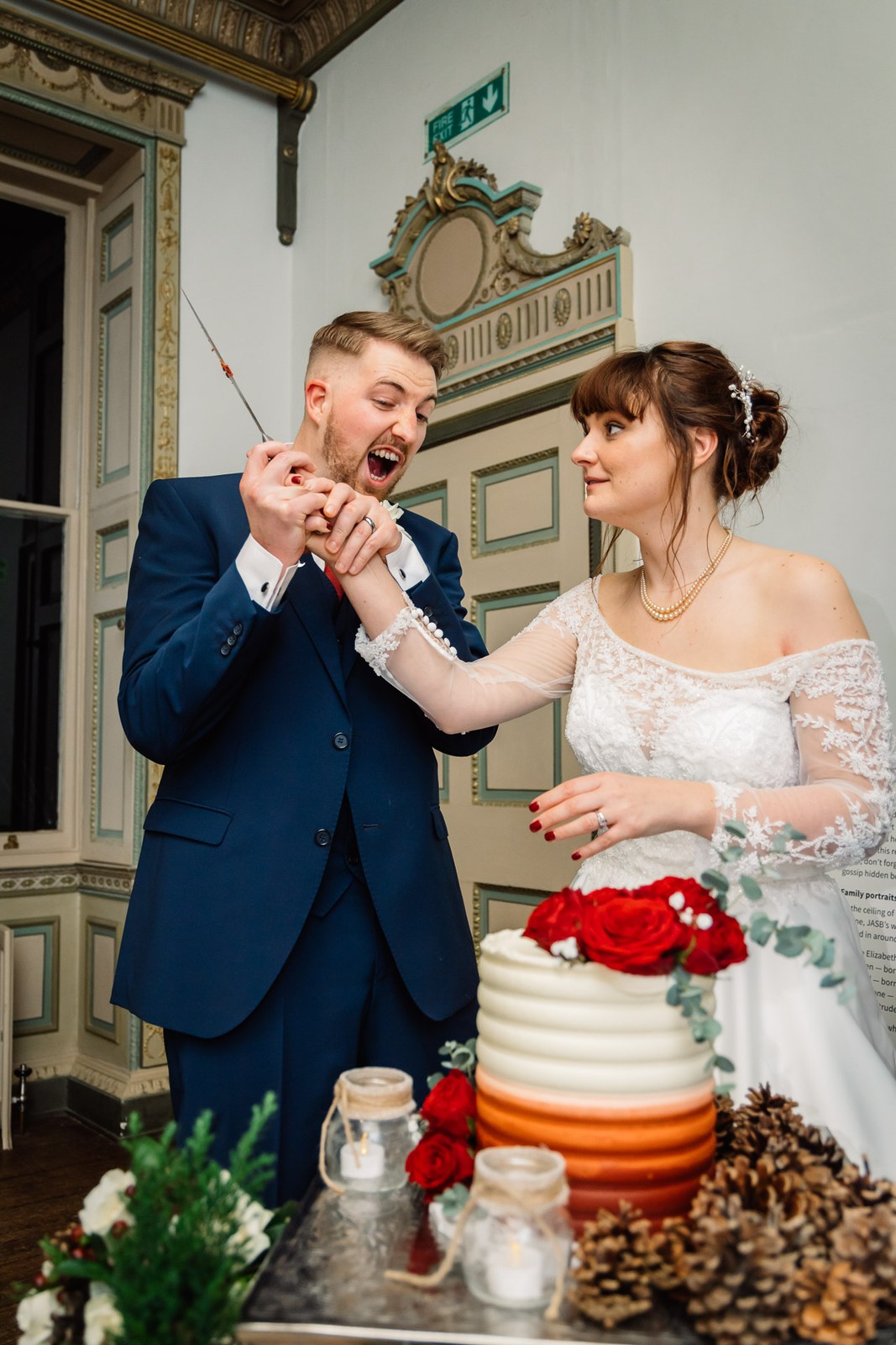 The couple laugh as they cut the cake, the groom pretending to bite the knife