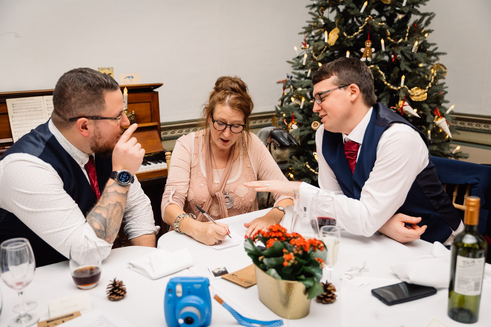 Three guests write at the table by the Christmas tree, an instant camera beside them