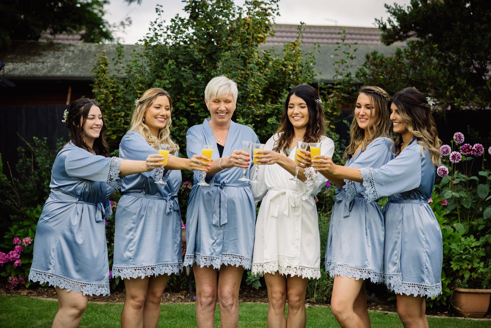 Bridesmaids and the mother of the bride in blue robes toasting with juice in the garden