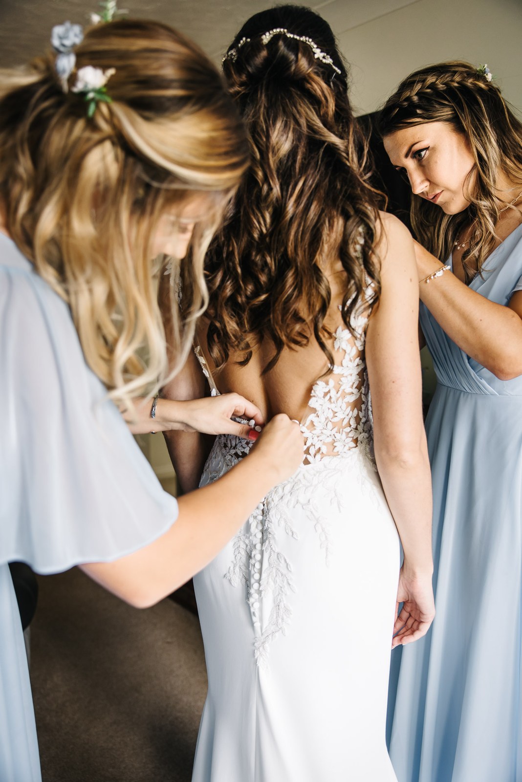 Bridesmaid fastening the buttons at the back of the bride's lace wedding dress