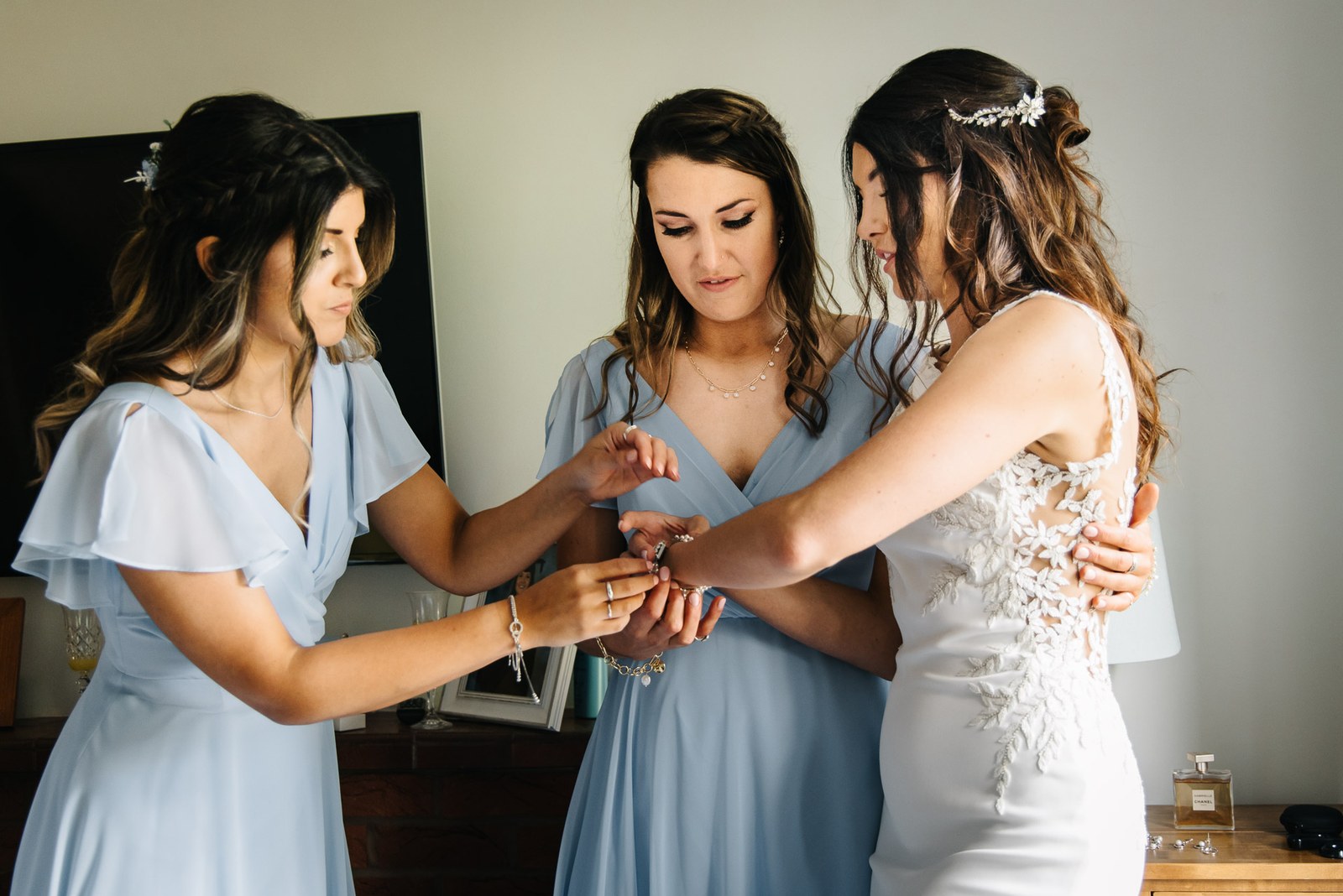 Bridesmaids helping the bride into her jewellery as she finishes getting ready