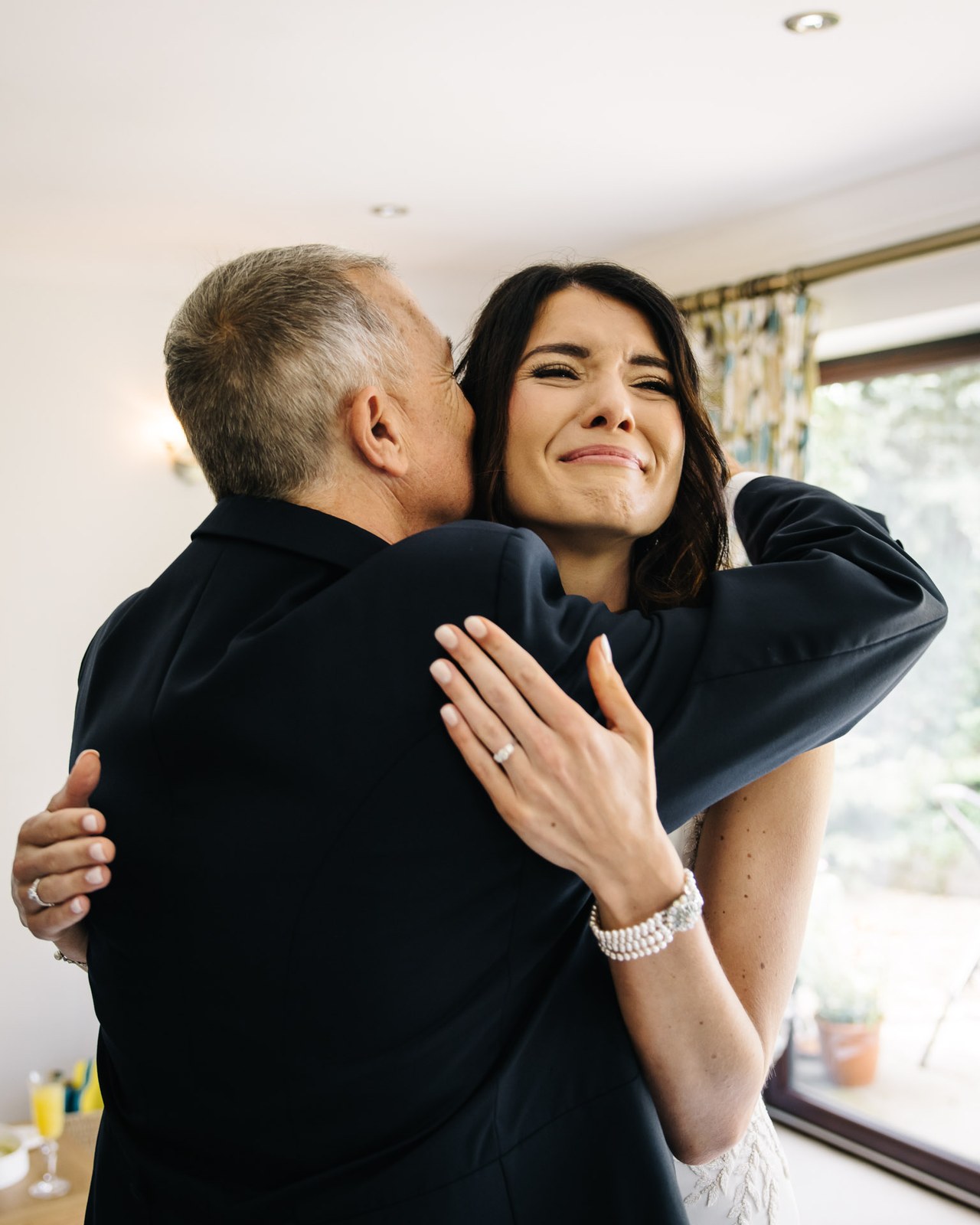 Father of the bride kissing his tearful daughter's cheek in a warm embrace