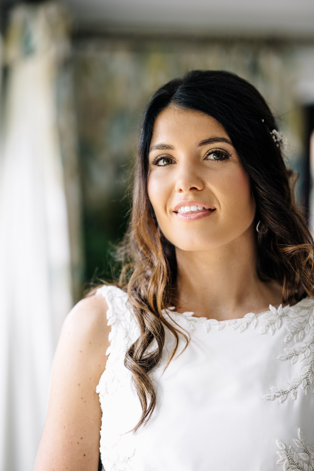 Bridal portrait, the bride smiling softly with a delicate hairpiece and lace neckline