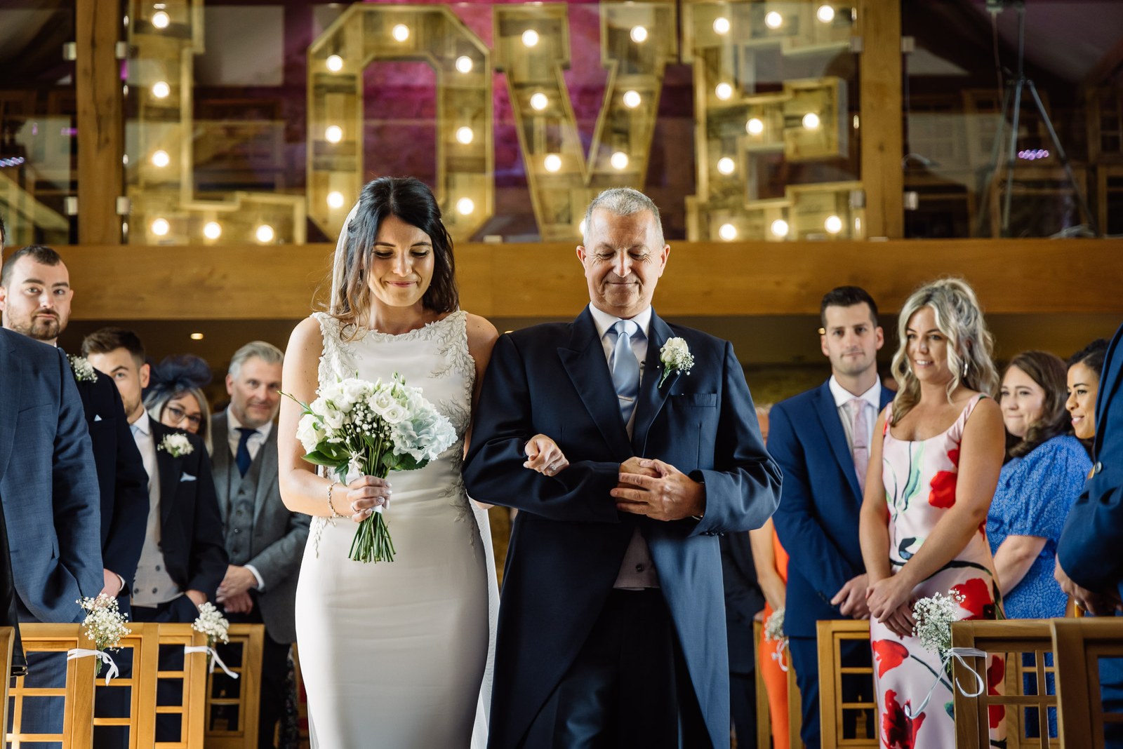 Bride walking the aisle on her father's arm beneath illuminated LOVE letters at Dodford Manor