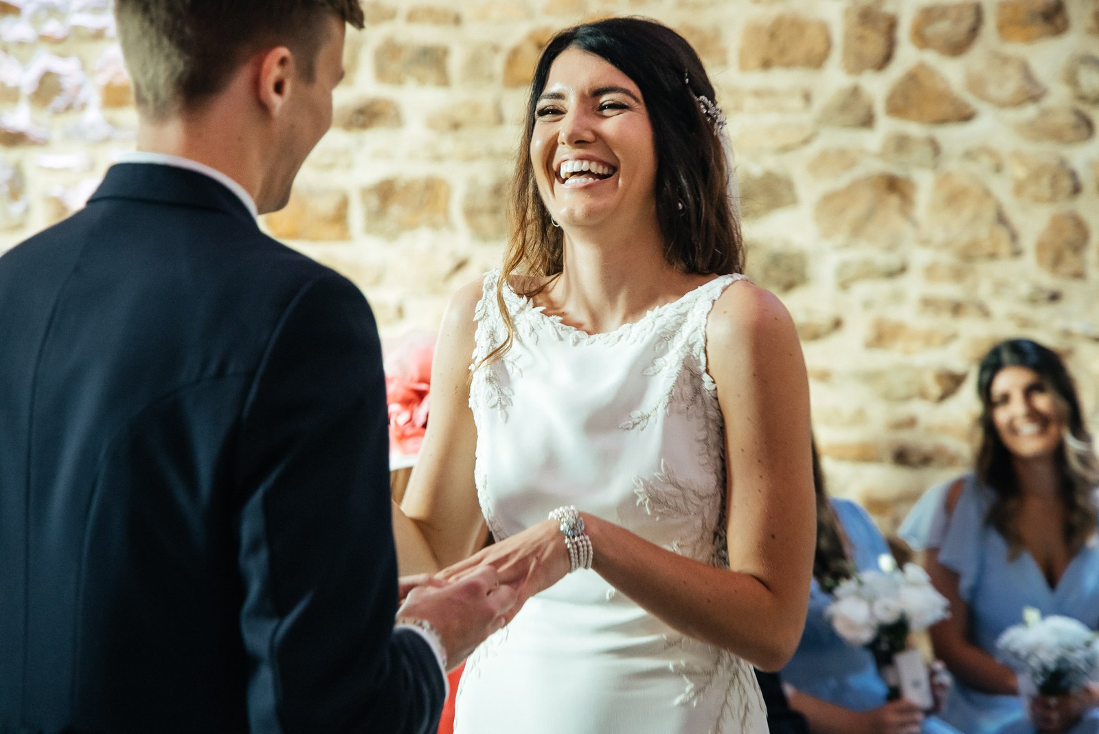 Bride laughing during the ceremony against the honey-stone barn wall