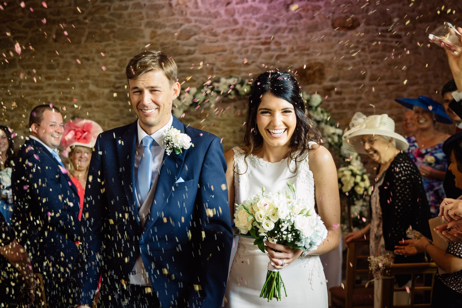 Newlyweds showered with confetti walking through the stone barn at Dodford Manor