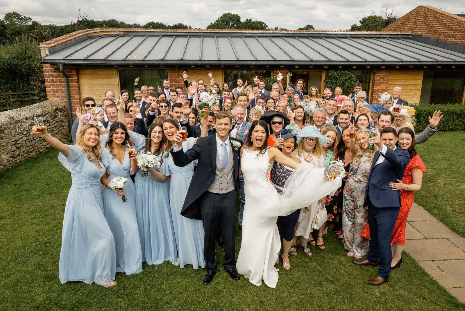 The full wedding party gathered outside the barn at Dodford Manor, waving to camera