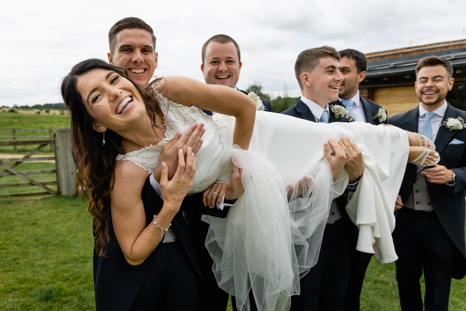 Groomsmen lifting the laughing bride aloft on the lawn