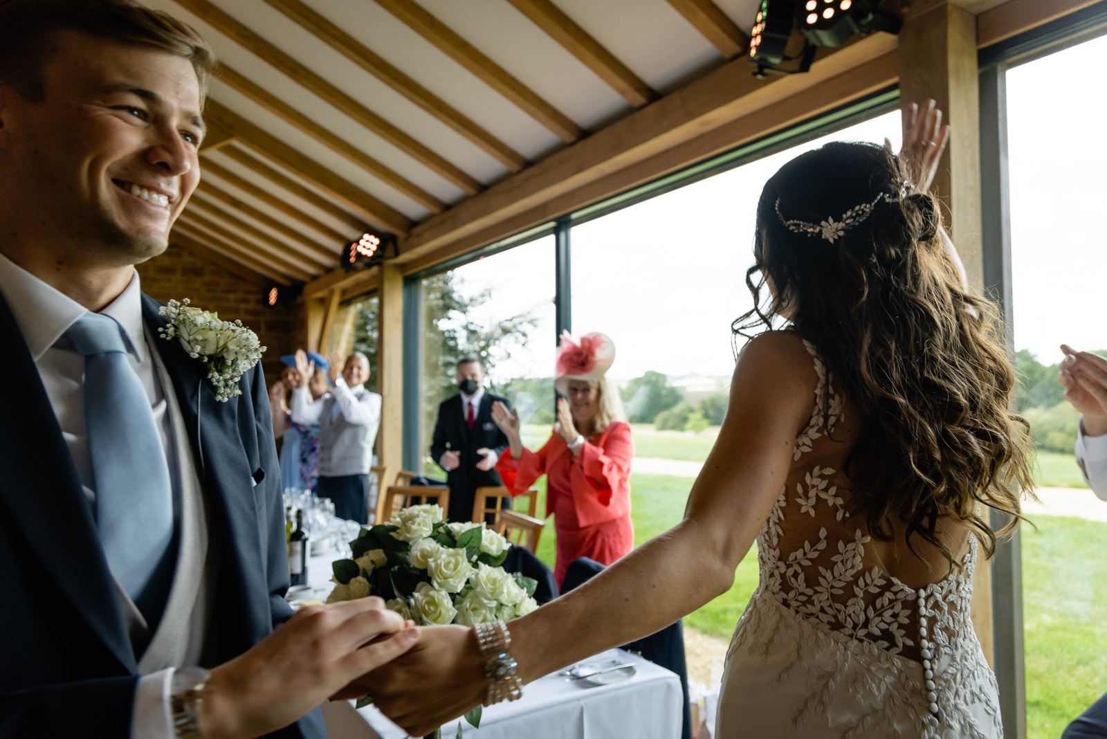 Groom taking the bride's hand across the top table in the oak-beamed room at Dodford Manor