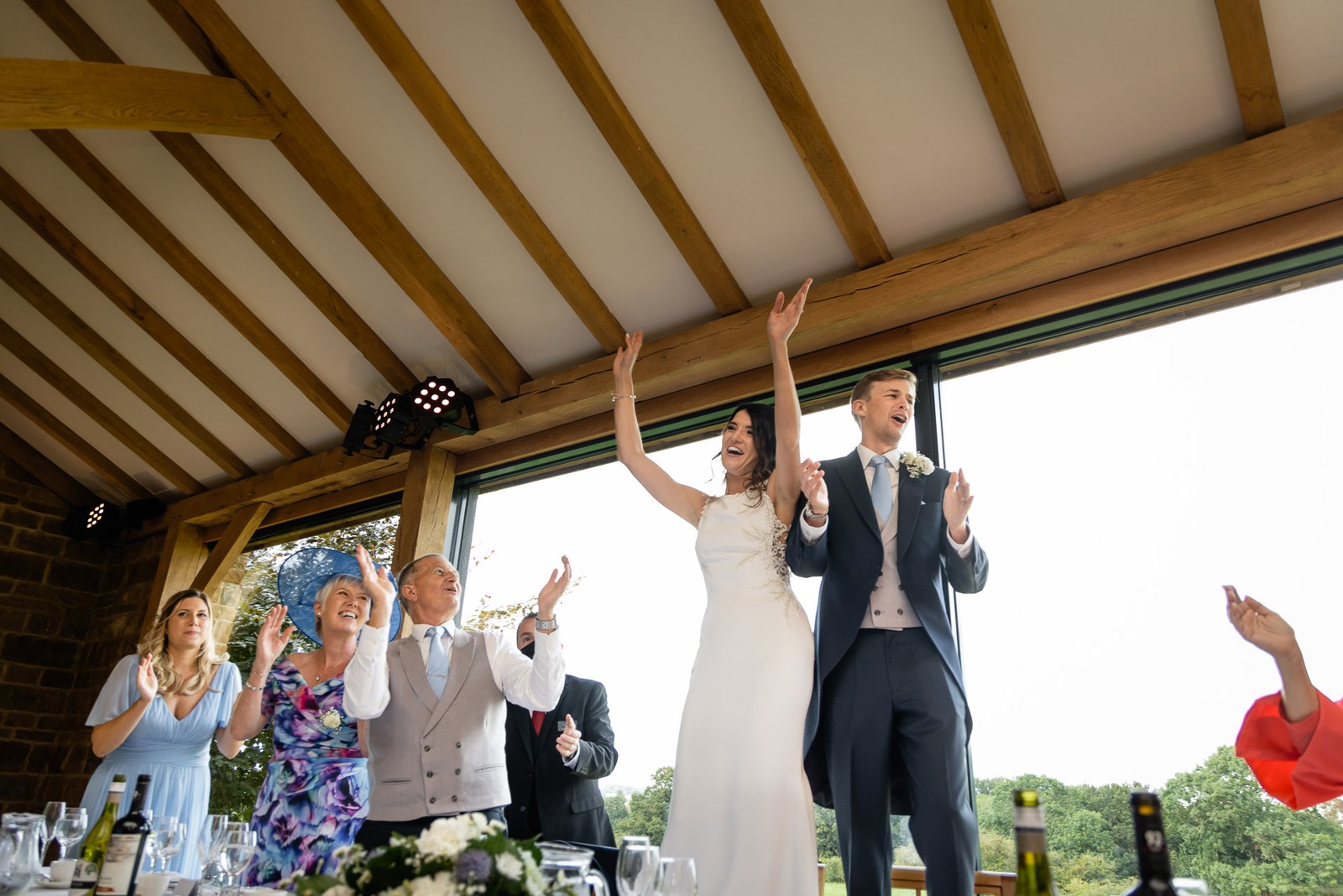 Bride and groom raising their arms in celebration at the top table as guests cheer