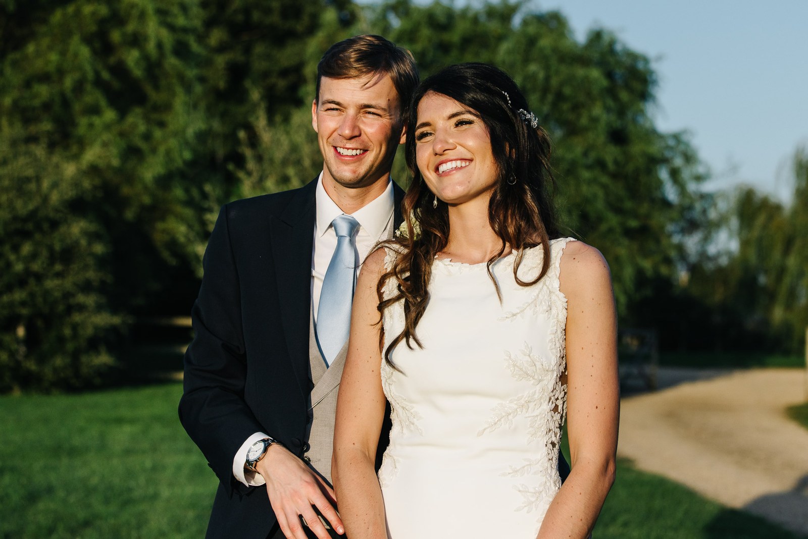 The couple smiling together in the golden evening light among the trees