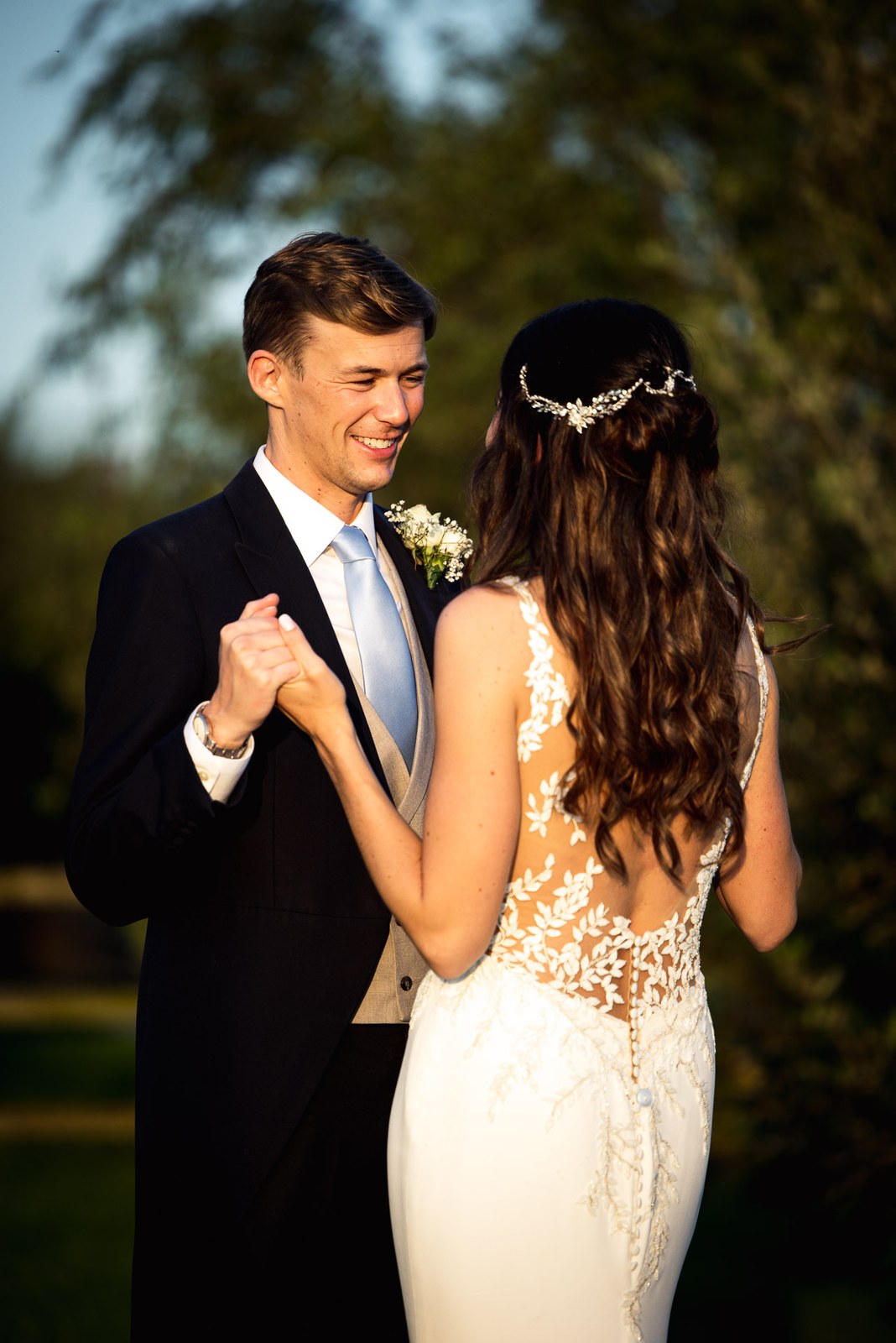 The couple dancing hand in hand beneath the trees in warm evening light