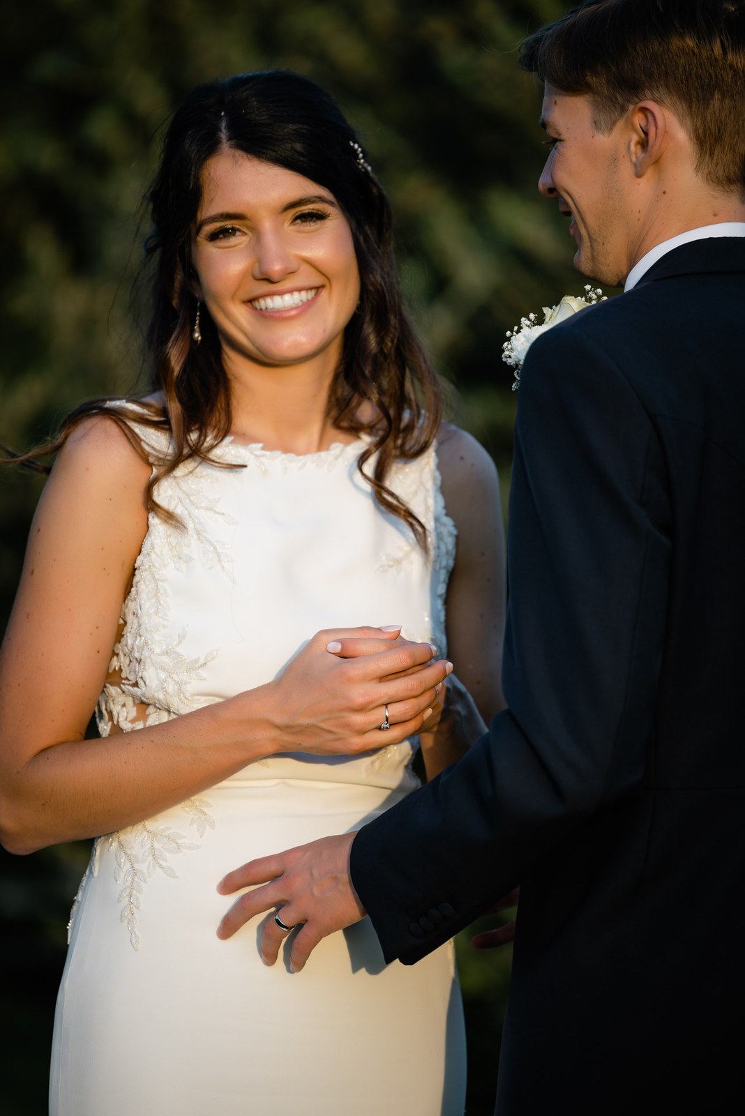 Bride smiling as the groom holds her close in the golden evening light