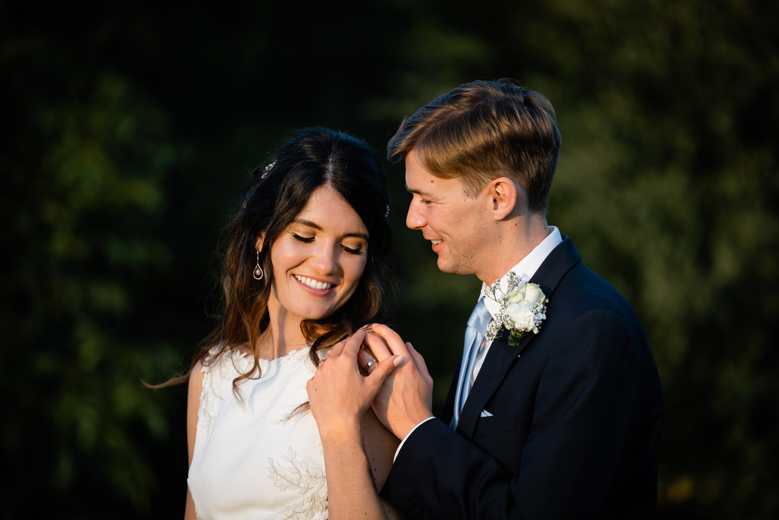 Groom holding the bride's hand between his own as she looks down, smiling