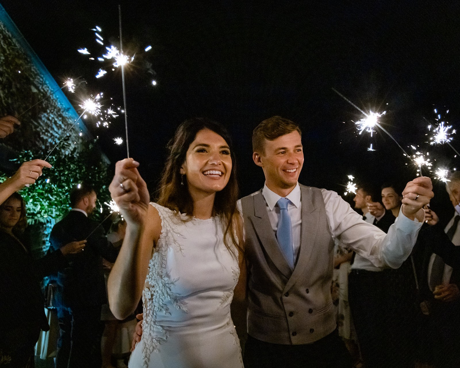 Newlyweds walking through a sparkler tunnel in the grounds of Dodford Manor at night
