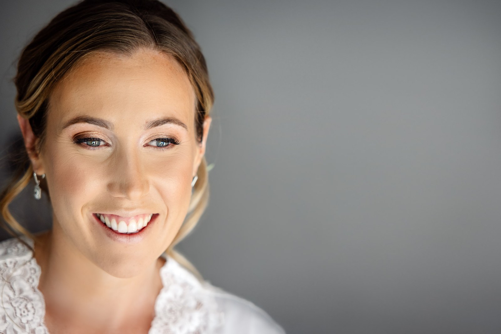 Bridal makeup portrait, the bride smiling with soft waves and a lace neckline