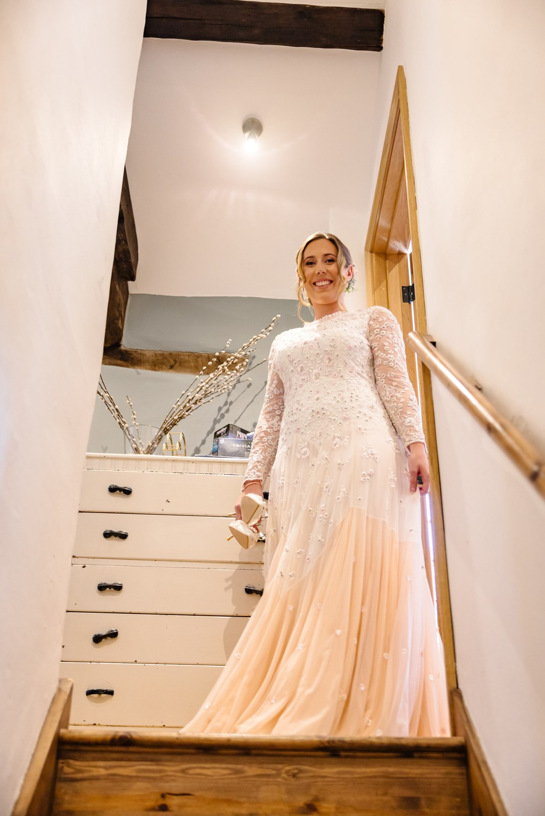 Bride in a blush gown pausing at the top of a cottage staircase