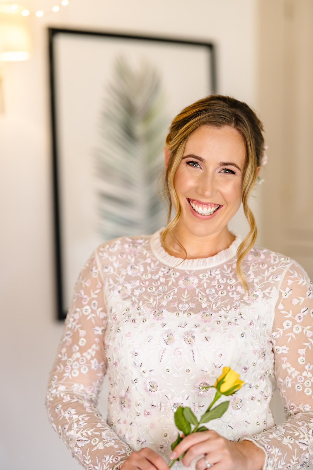 Bride in a beaded lace gown holding a single yellow flower for a portrait