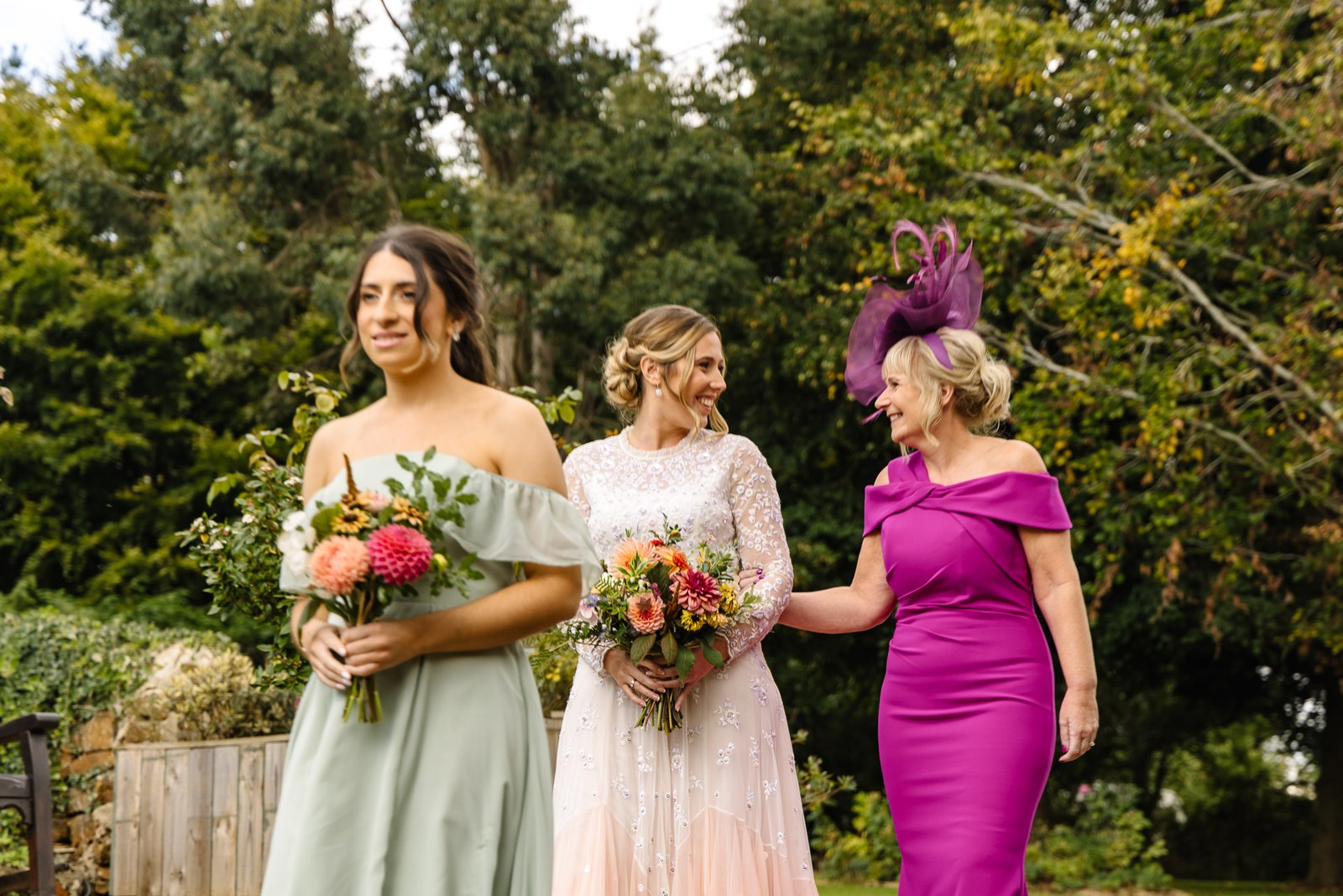Bride and a bridesmaid with the mother of the bride among the trees, bouquets in hand