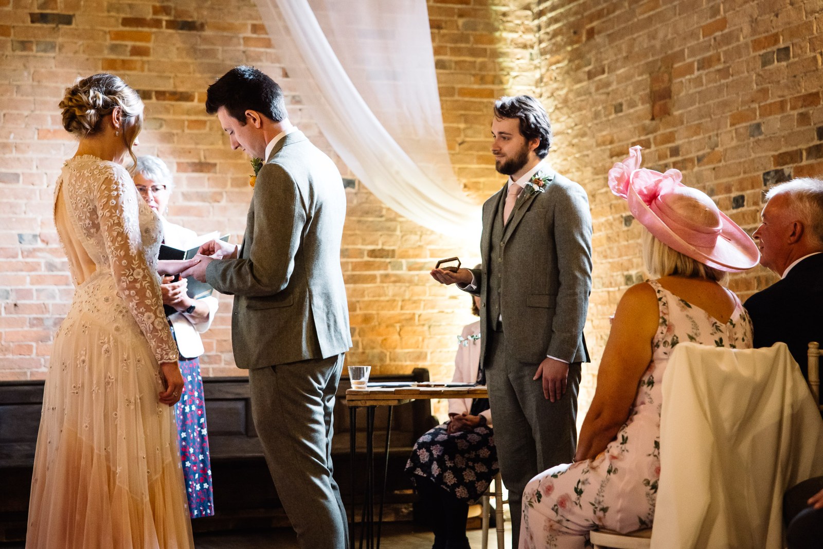 Bride and groom exchanging rings before the celebrant in the barn at Dovecote Events