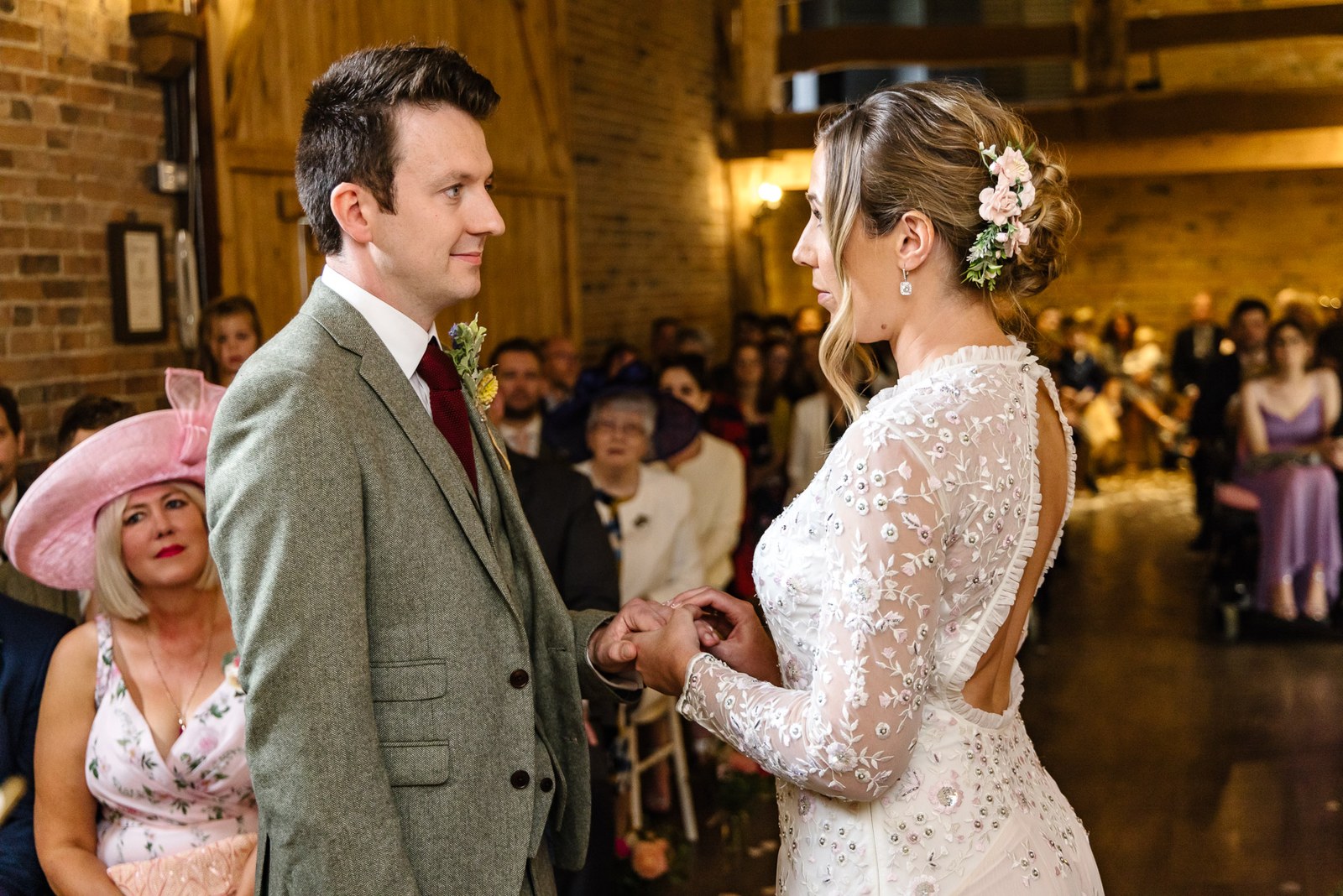 Bride placing the wedding ring on the groom's finger as guests look on