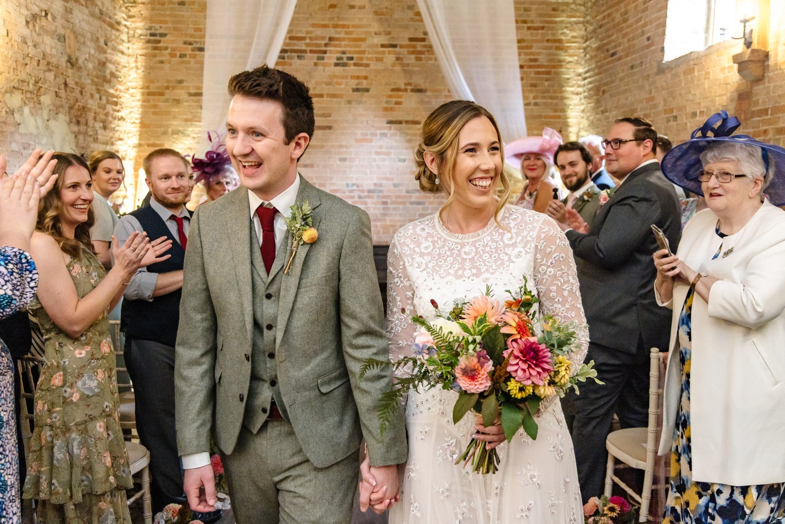 Newlyweds walking back down the aisle to applause, the bride holding an autumnal bouquet