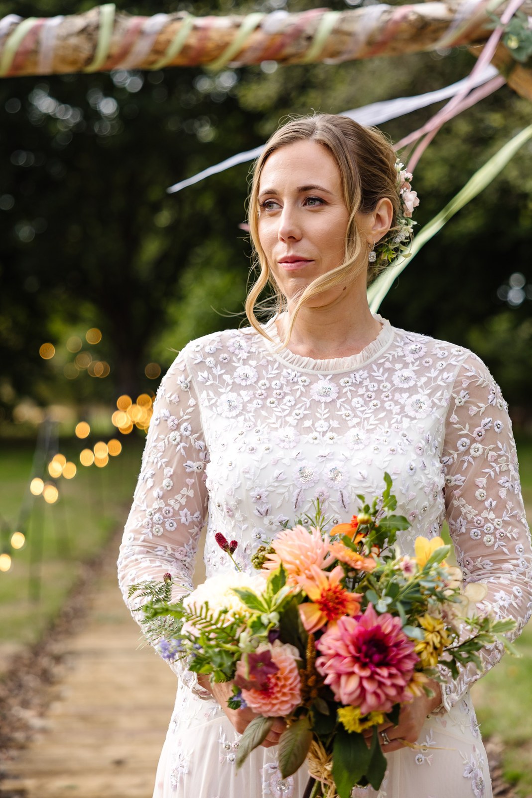 Bride beneath the ribboned wooden arch, holding a warm-toned autumn bouquet