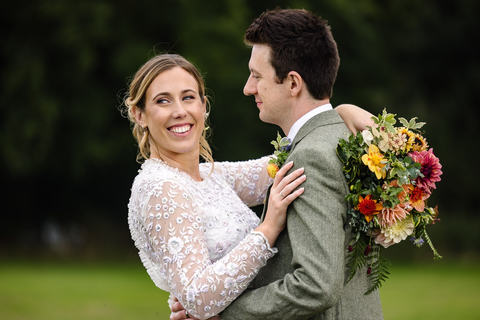 The groom smiling at his bride as she holds her bouquet among the greenery