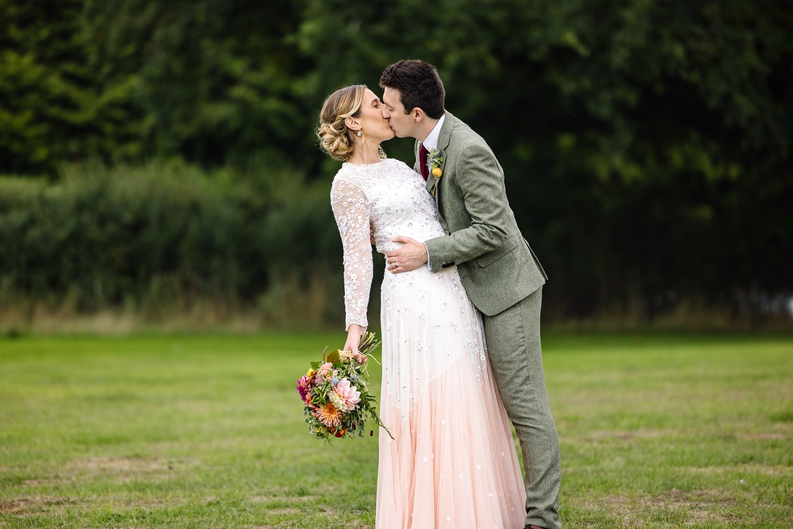 The couple sharing a kiss on the lawn, the bride's blush-hemmed gown catching the light