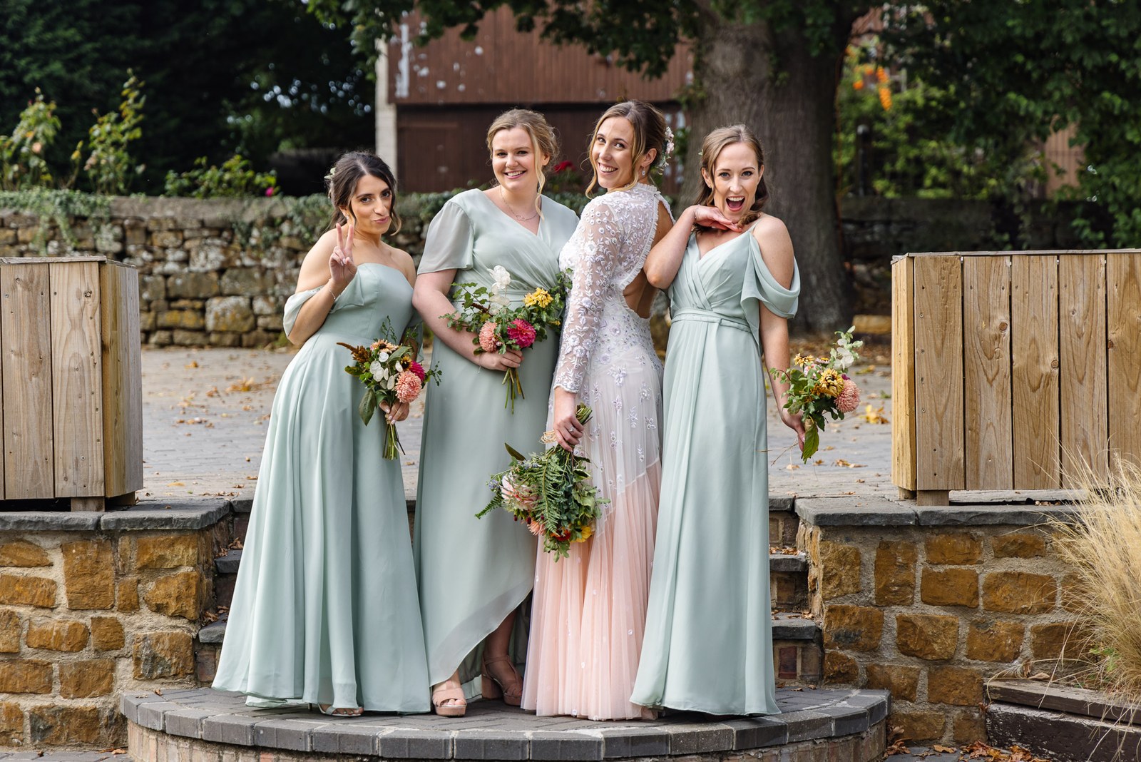 Bridesmaids and the bride on the stone terrace at Dovecote Events, bouquets in hand