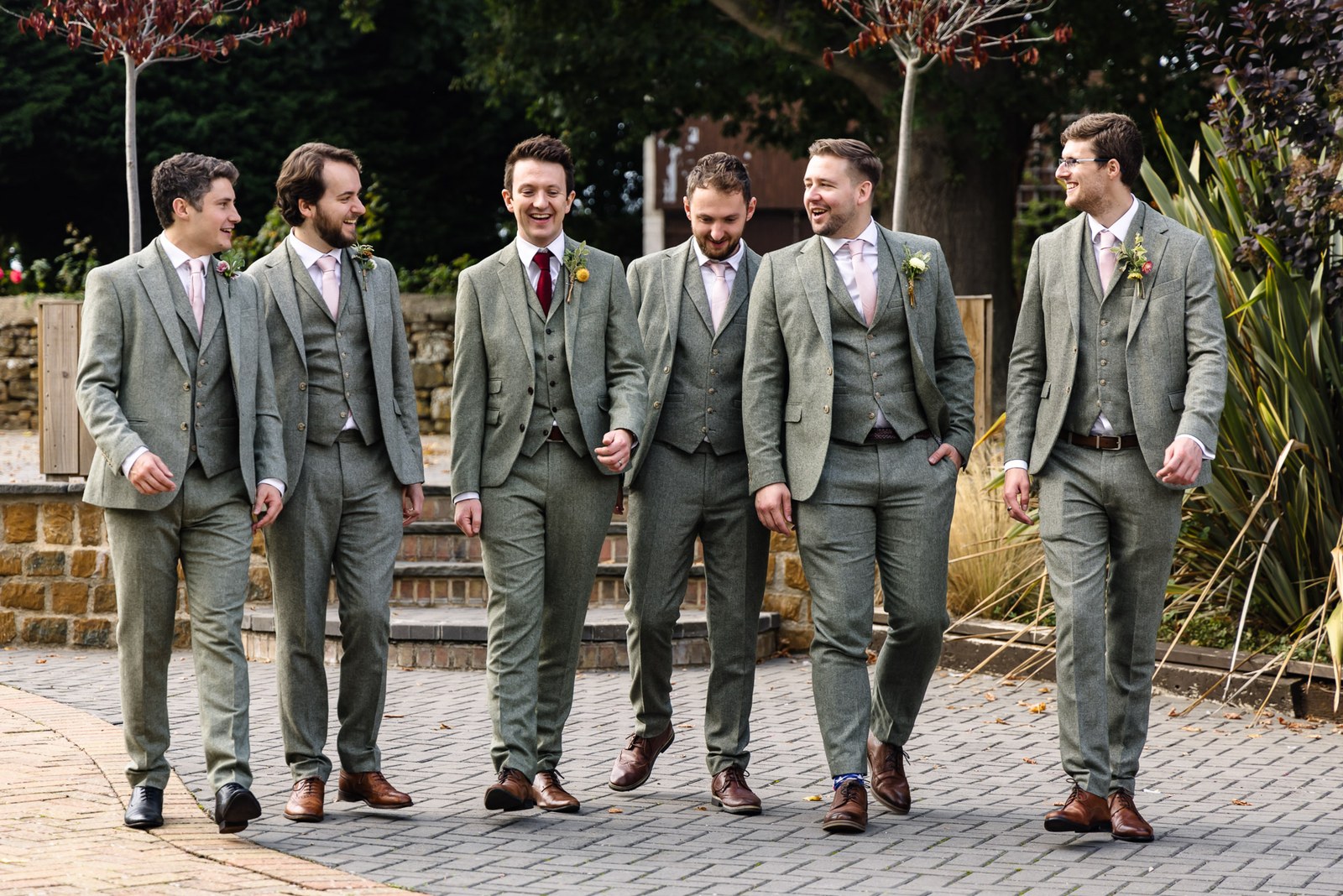 The groom and his groomsmen in sage-green suits walking down the stone steps together