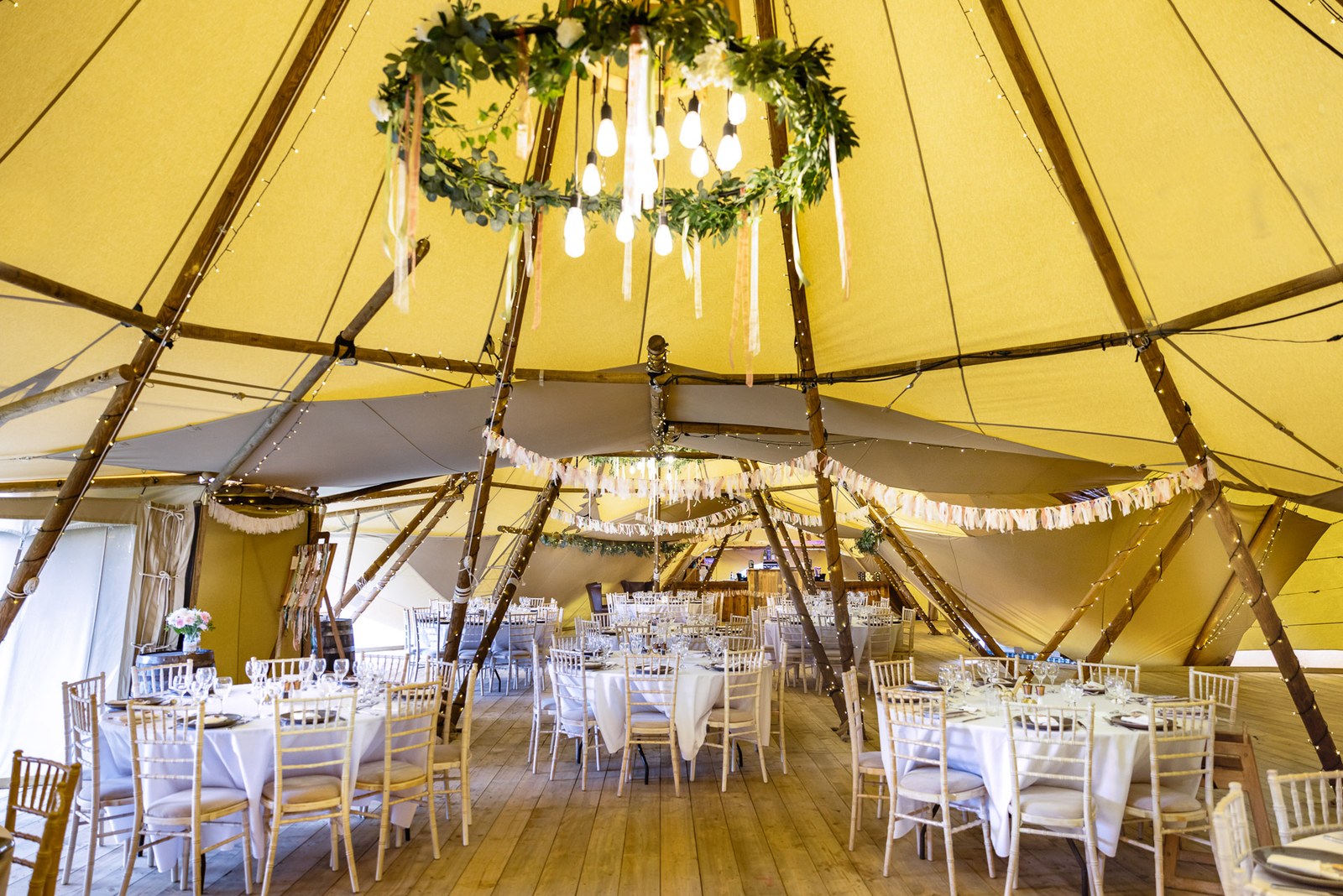 Inside the tipi at Dovecote Events, a foliage chandelier and fairy lights above set tables