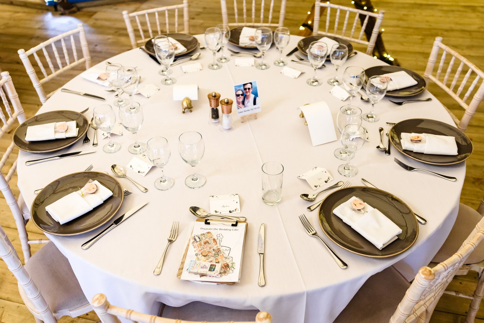 A round reception table laid with dark plates, place cards and a photo table centre