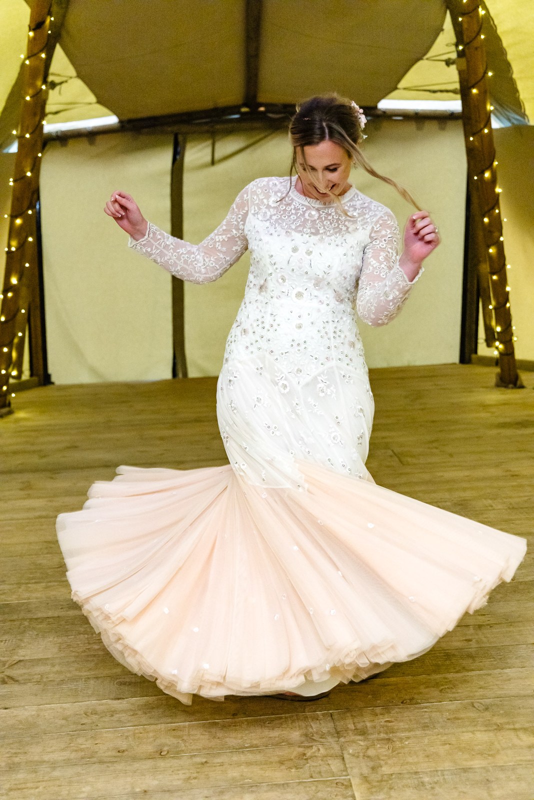 Bride twirling her blush-hemmed gown inside the fairy-lit tipi at Dovecote Events