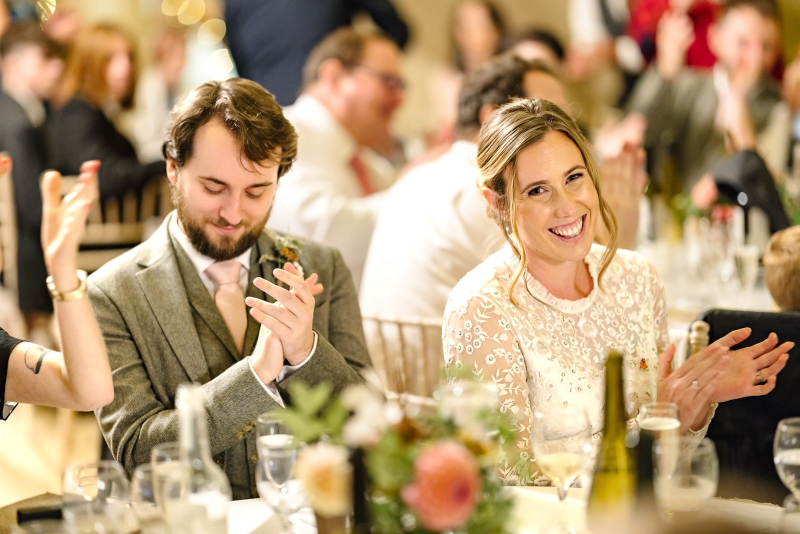 Bride and a groomsman applauding at their table during the speeches