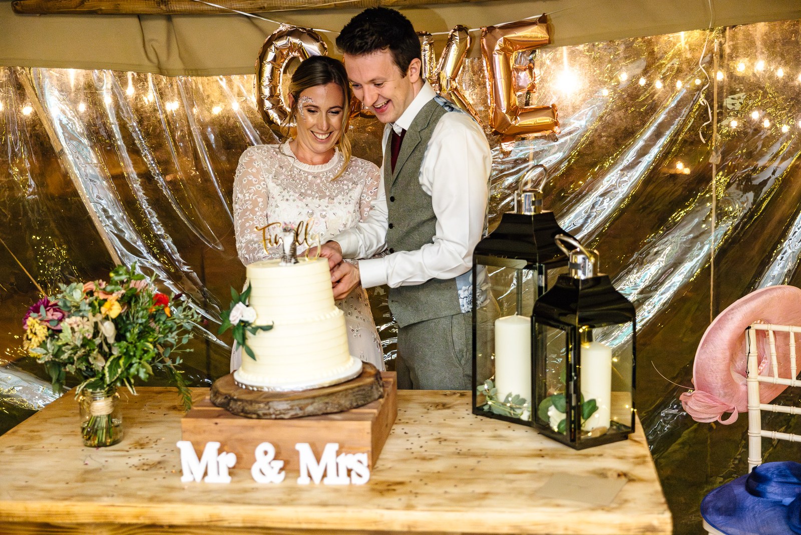 The couple cutting their cake beside a 'Mr and Mrs' sign and gold balloons among lanterns