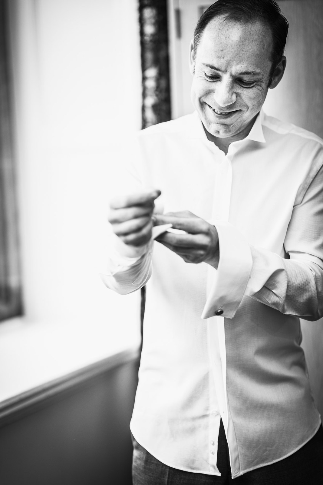 Black-and-white of the groom fastening a cufflink, smiling to himself