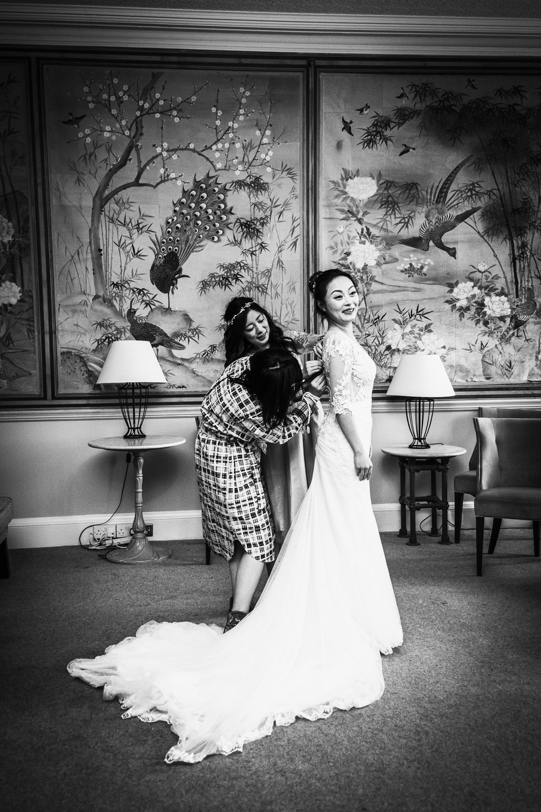 Black-and-white of the bride's gown train being arranged in the panelled room