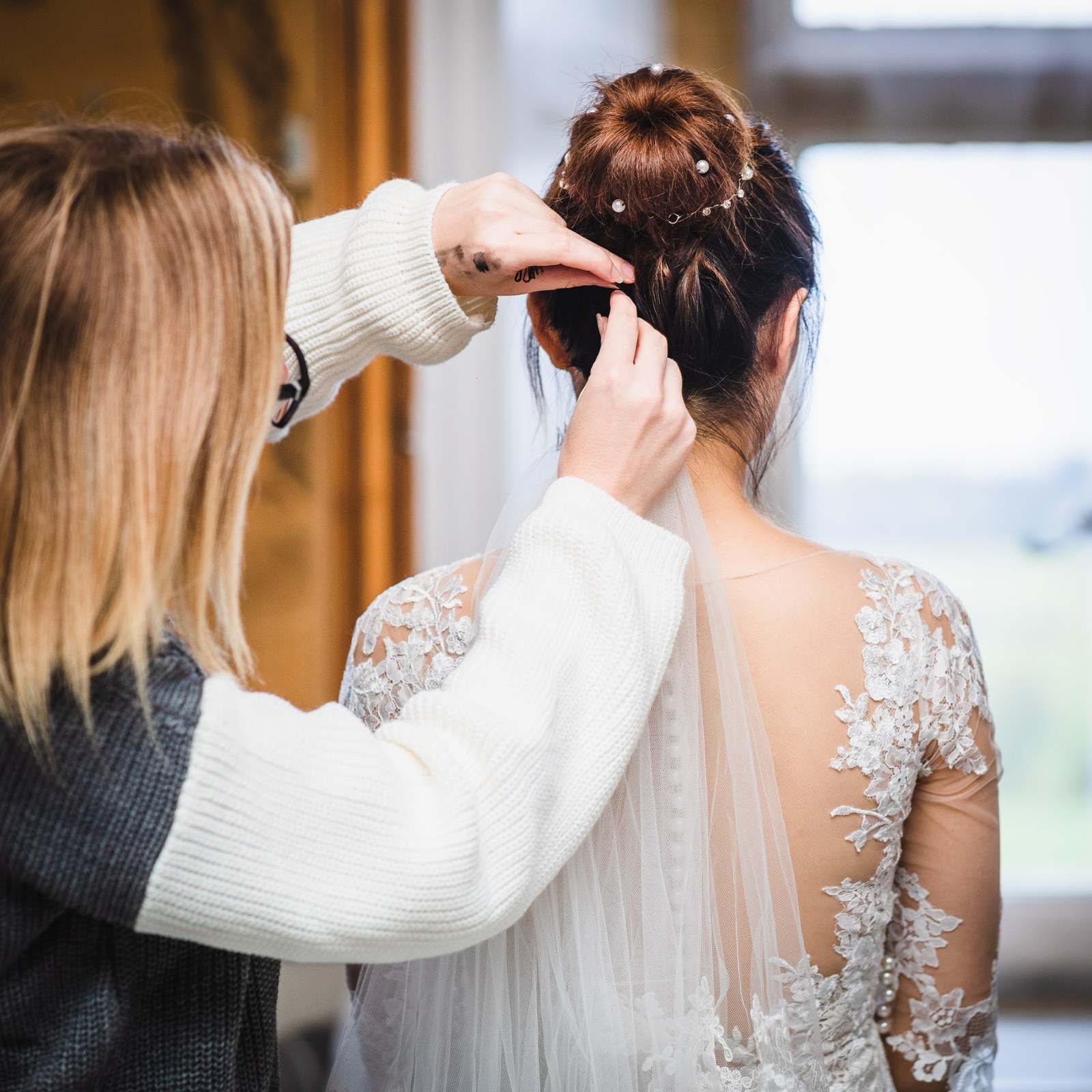 A stylist pinning the veil into the bride's high bun, seen from behind