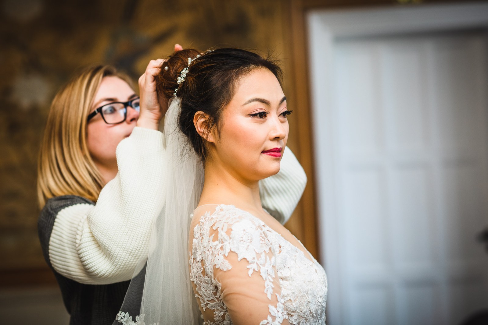 A stylist fixing the bride's hair as she waits in profile against gold wallpaper
