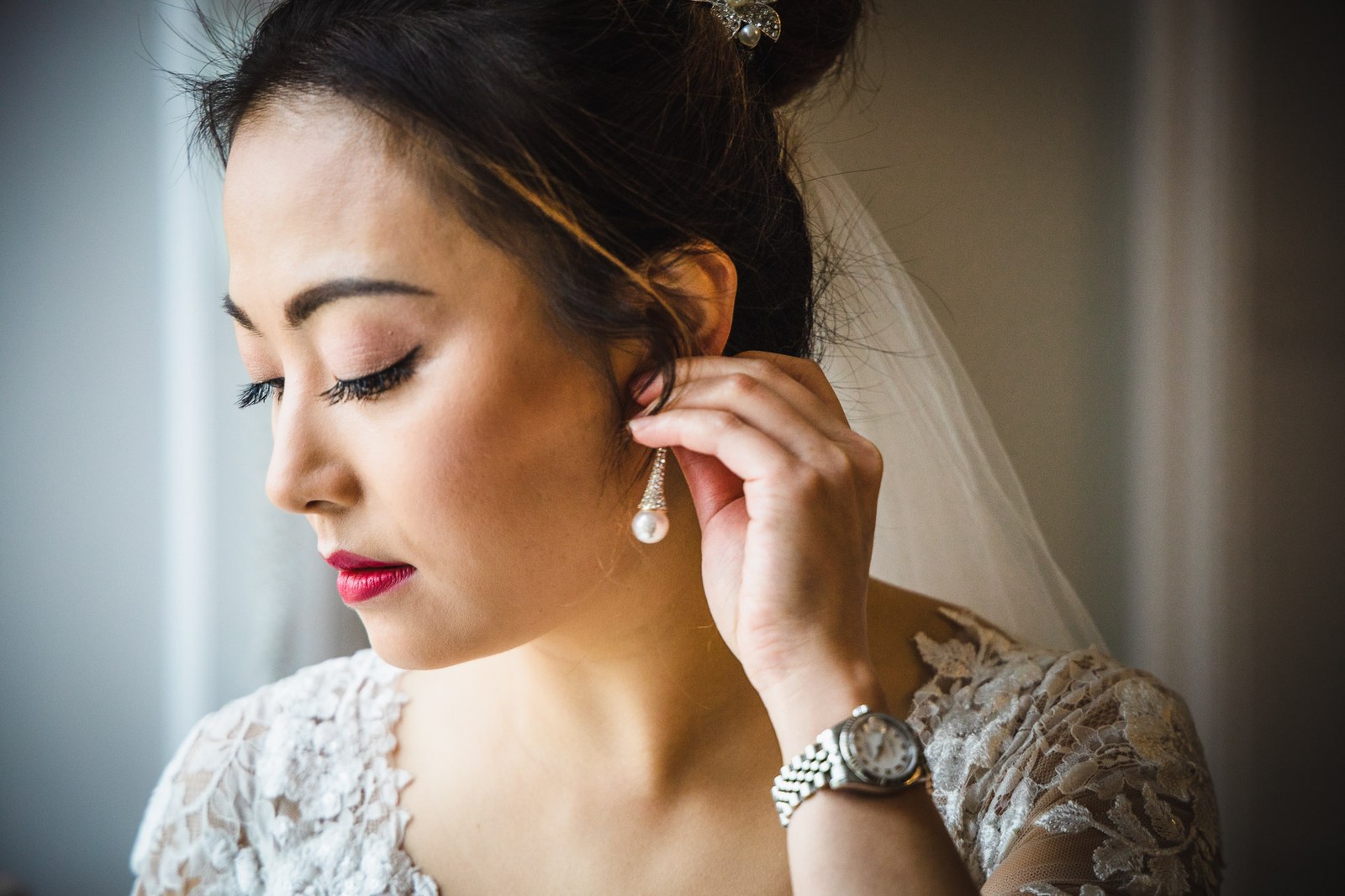 The bride fastening a pearl drop earring in soft window light