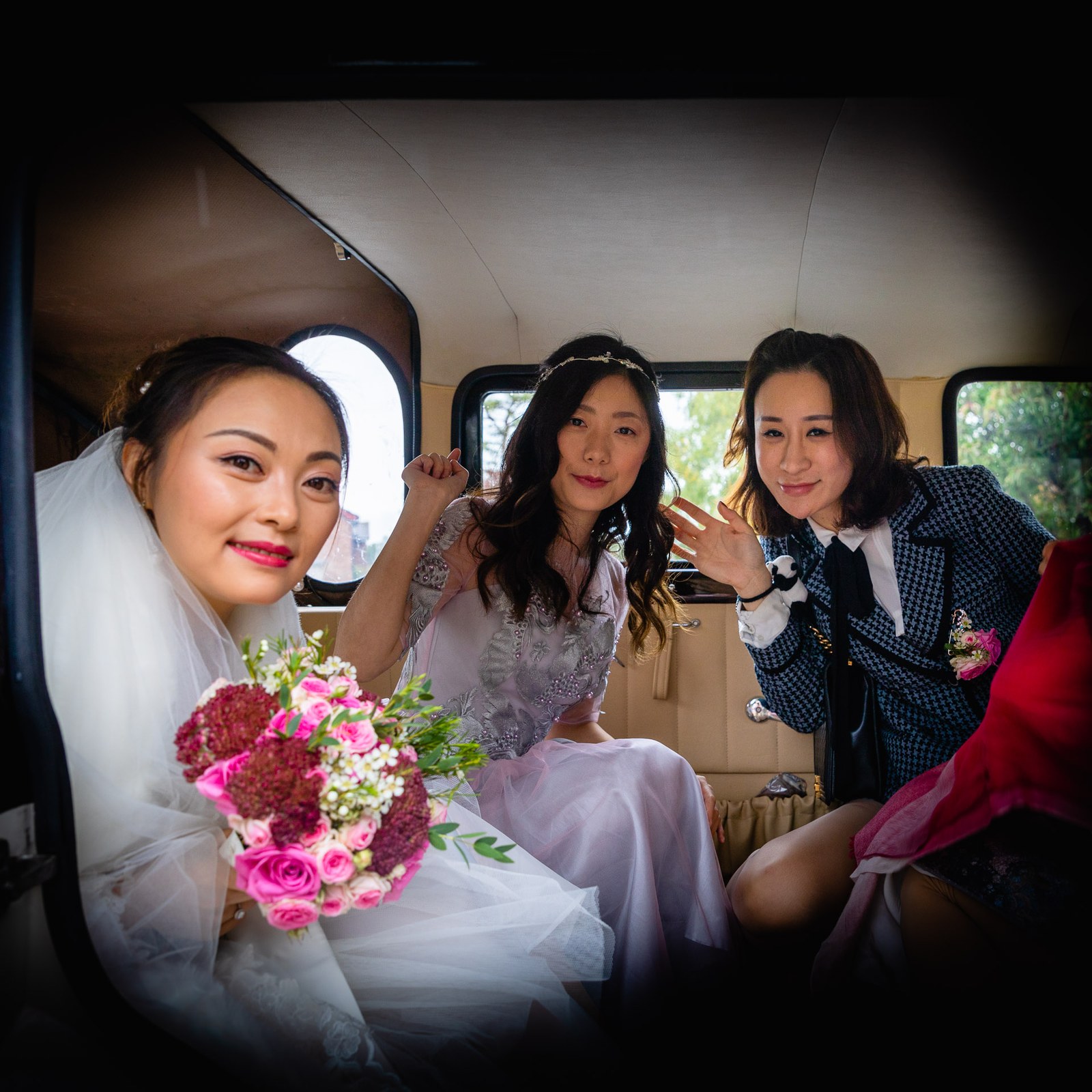 Bride with two of her bridal party in the wedding car, one waving to the camera