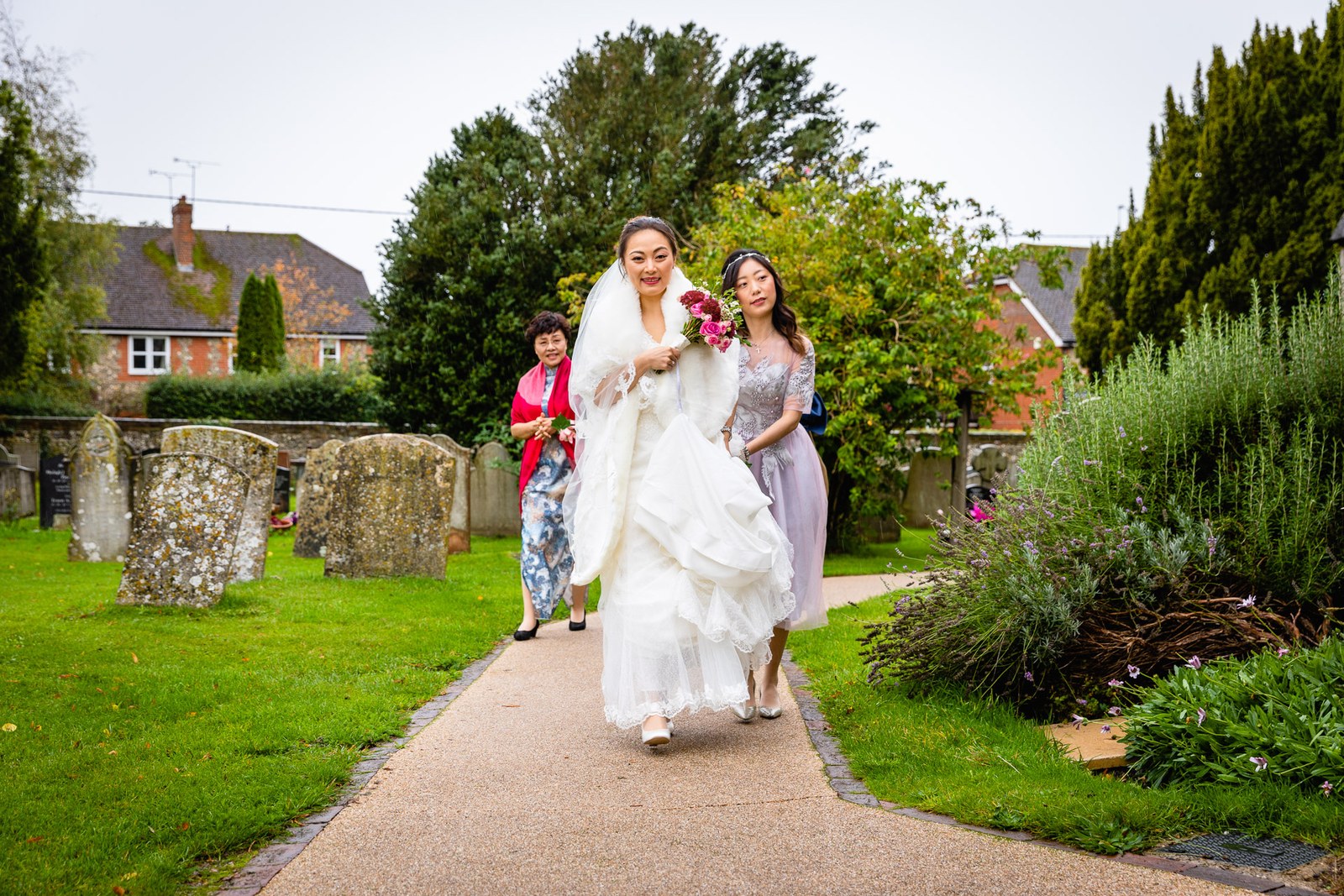 Bride arriving along the churchyard path, escorted past weathered gravestones