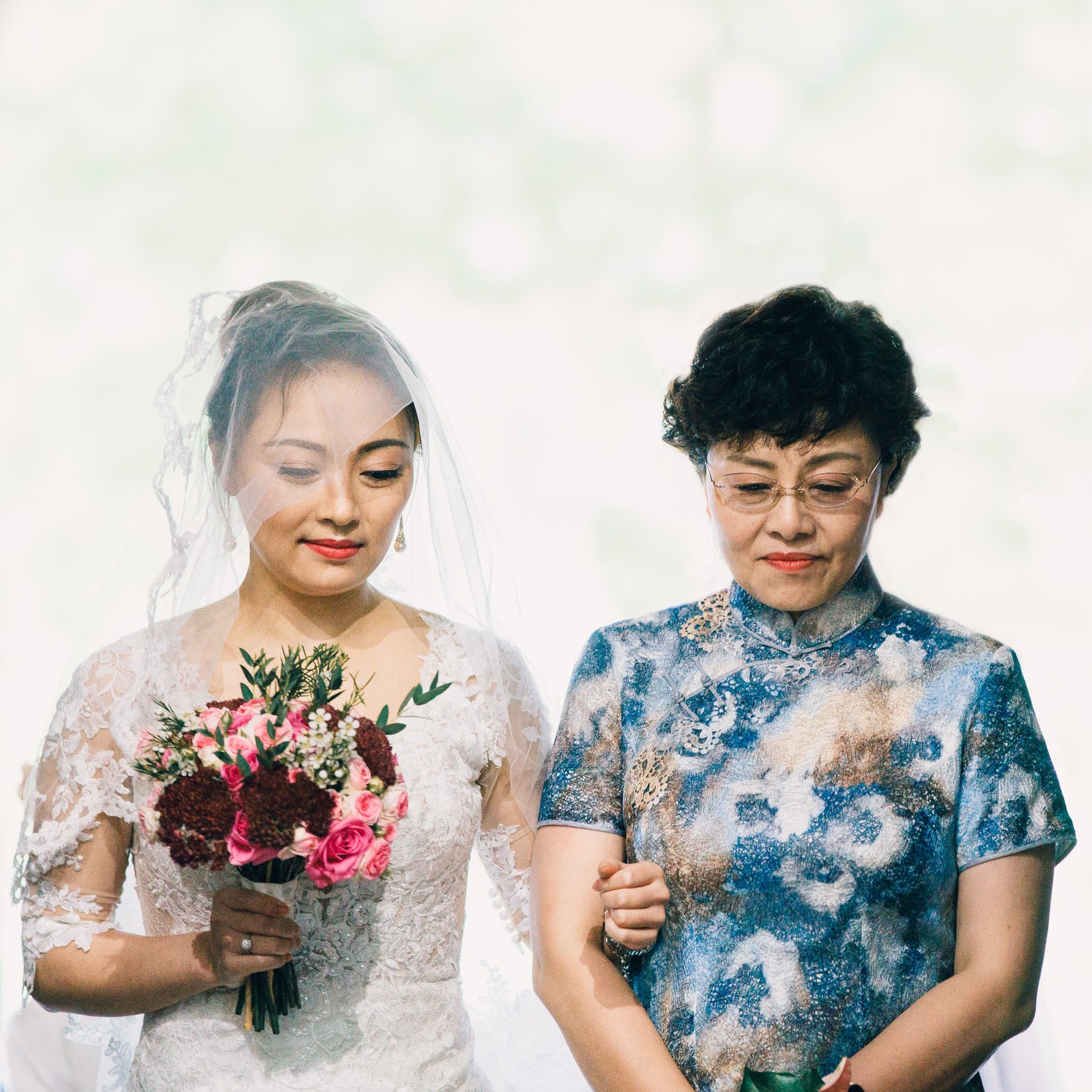 Bride walking toward the ceremony with her mother, veil trailing behind