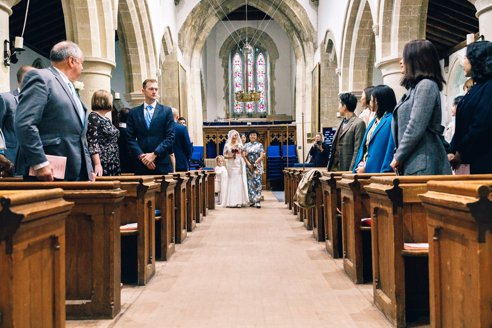 The view down the church aisle, guests standing as the bride reaches the altar