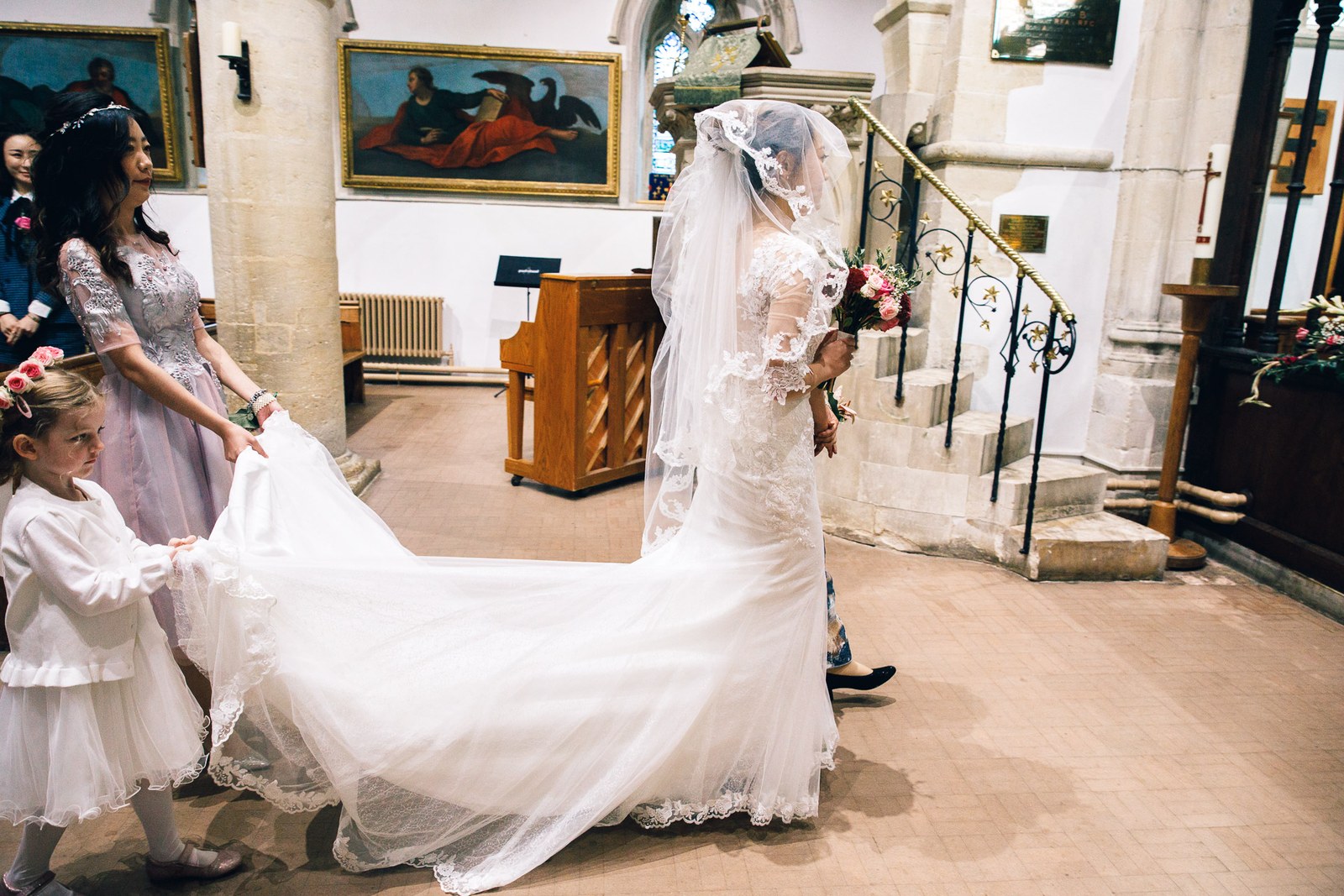 A young flower girl carrying the bride's long train at the altar