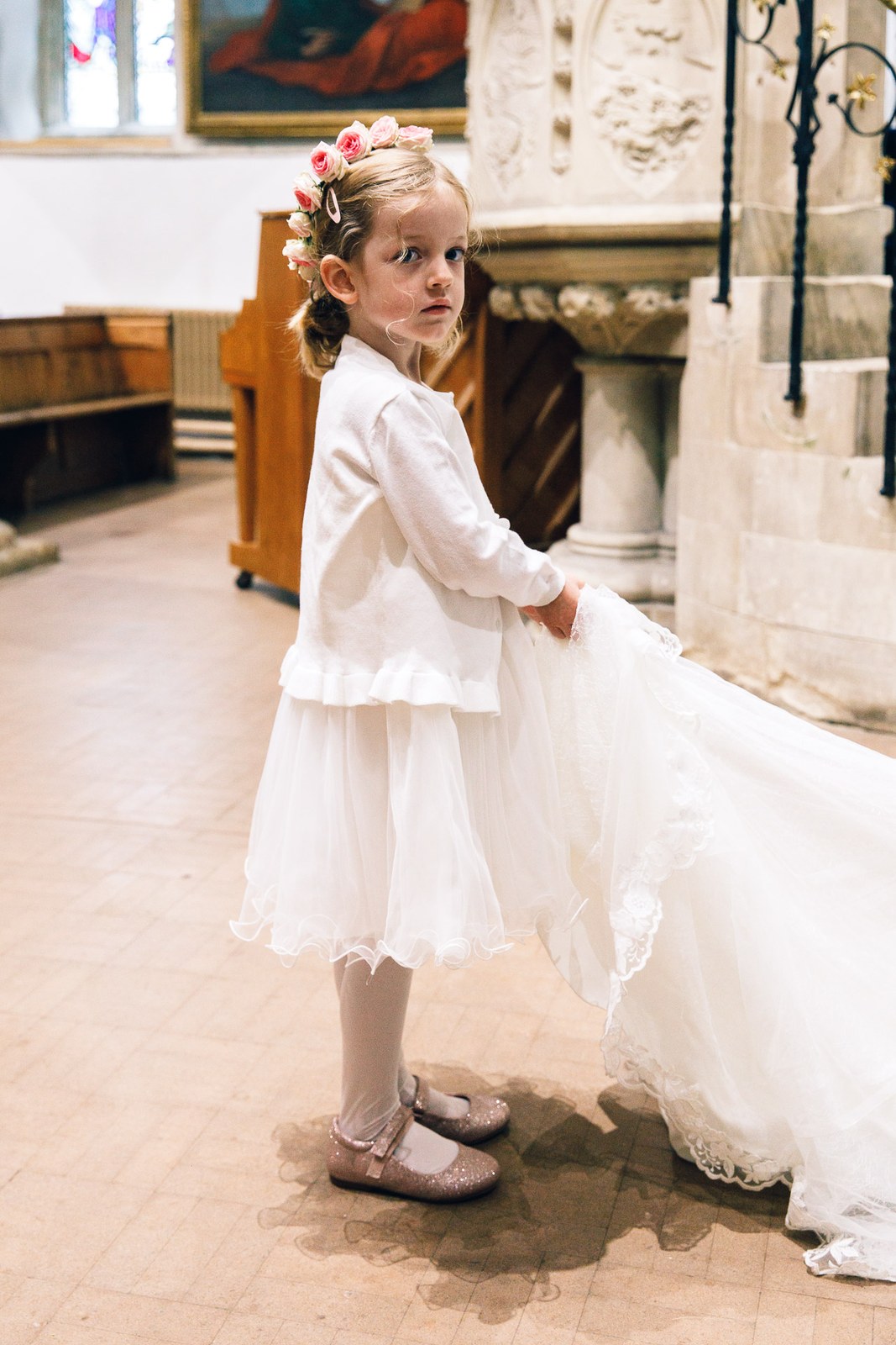 Flower girl in white glancing back as she holds the bride's veil and train