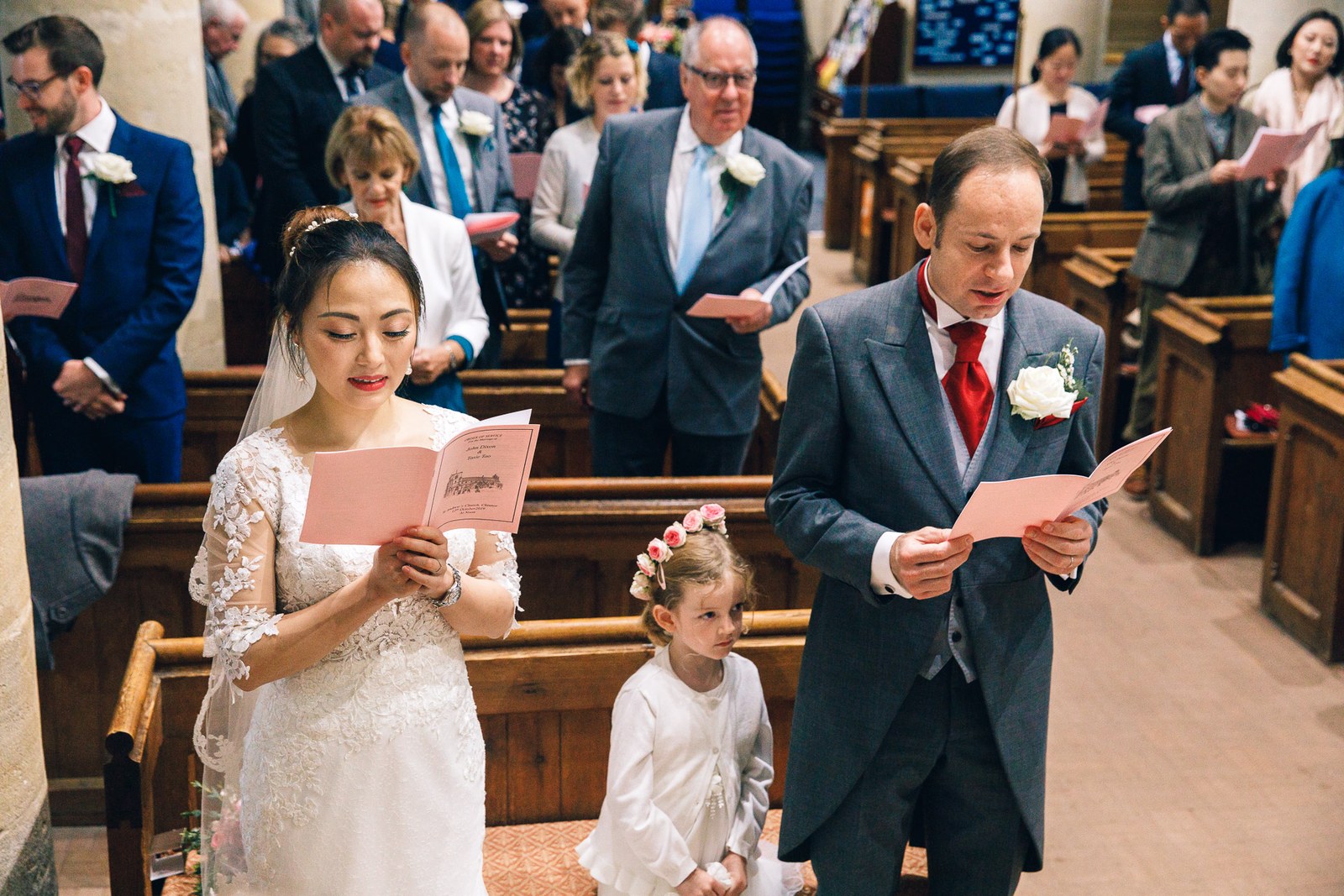 Bride and groom singing from pink hymn books, the flower girl standing between them