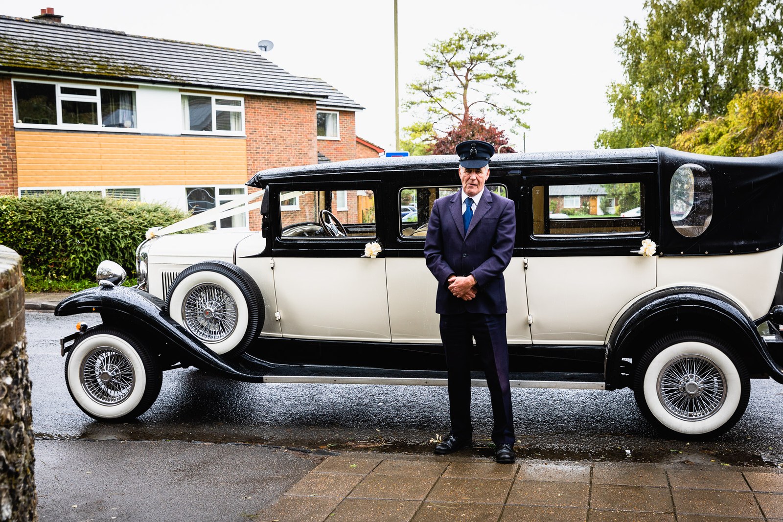 The vintage cream-and-black wedding car with its chauffeur standing by